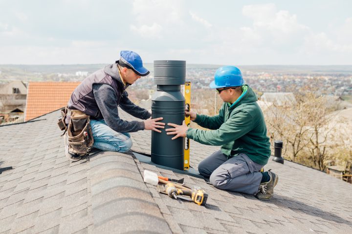 Chimney Repair - workers on the roof installing tin cap on the iron chimney. roofing Construction and Building New iron House with Modular Chimney,